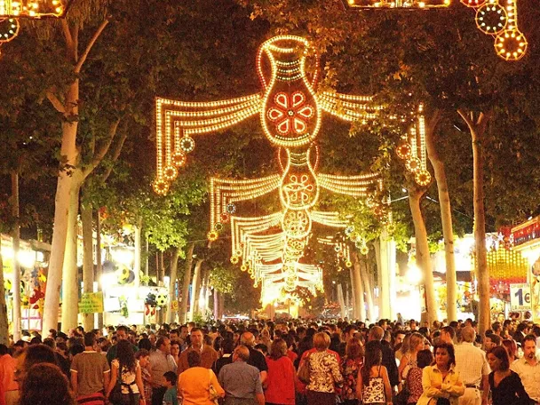 Paseo arbolado con iluminación festiva y gran afluencia de público.
