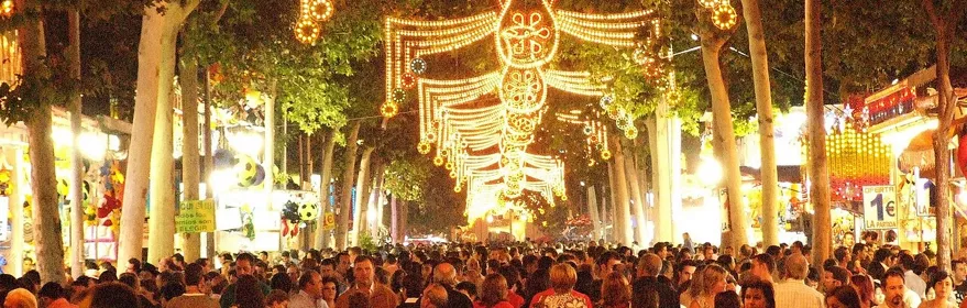 Paseo arbolado con iluminación festiva y gran afluencia de público.