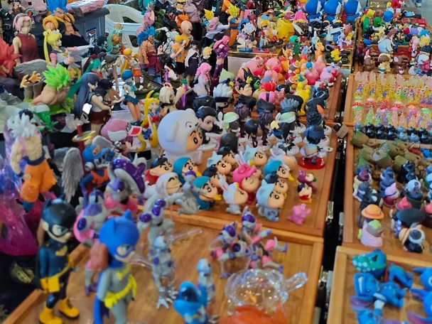 Mesa de exposición llena de figuras y muñecos de colores en un pabellón ferial.