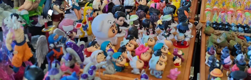 Mesa de exposición llena de figuras y muñecos de colores en un pabellón ferial.