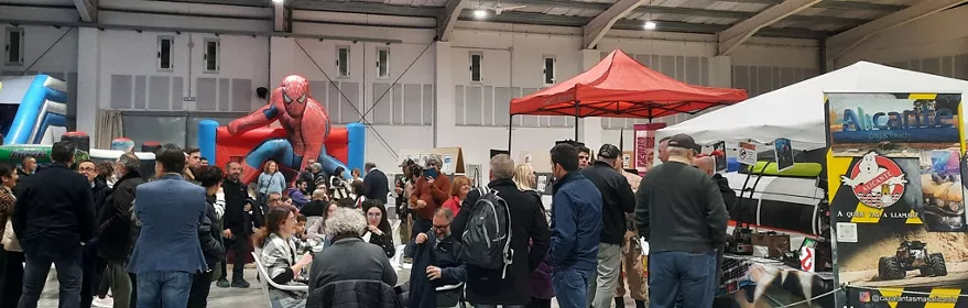 Público en feria de cómic en pabellón cubierto con figuras y puestos temáticos.