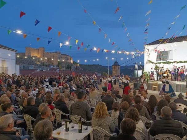 Festival al aire libre al atardecer con escenario, público sentado y guirnaldas de luces.