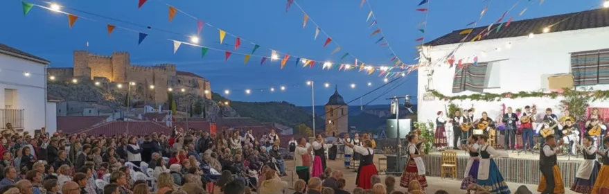 Festival al aire libre al atardecer con escenario, público sentado y guirnaldas de luces.