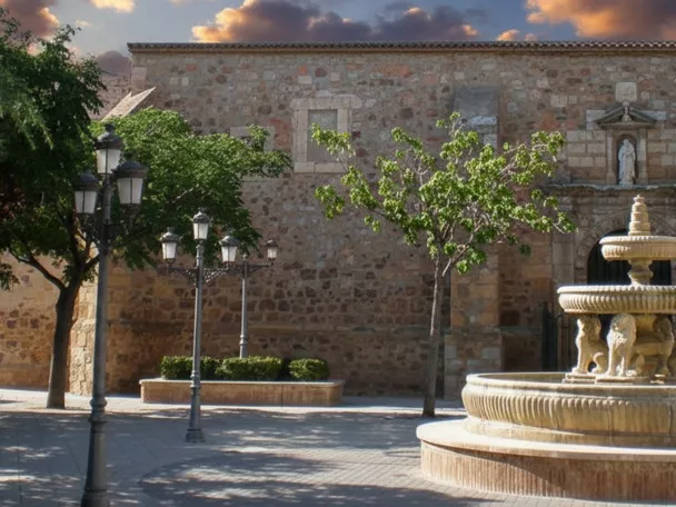 Plaza principal de Fernán Caballero (Ciudad Real) con fuente ornamental y fachada de la iglesia parroquial al fondo.