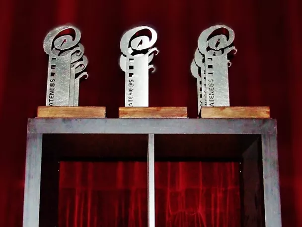 Trofeos plateados sobre mesa ante cortina roja