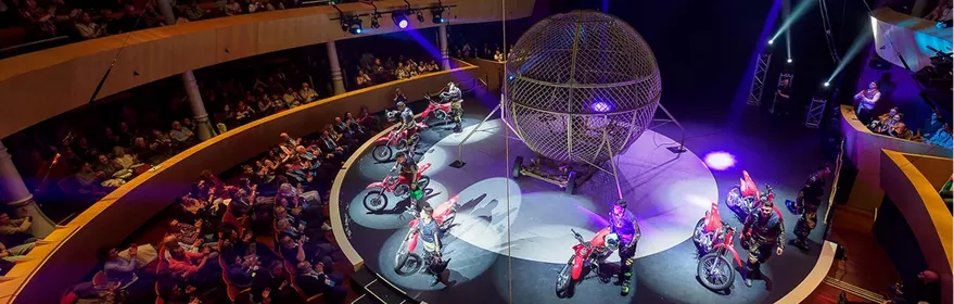Espectáculo circense con motoristas girando dentro de una esfera metálica ante público