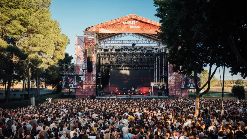 Gran concentración de personas frente a escenario en parque durante el día.