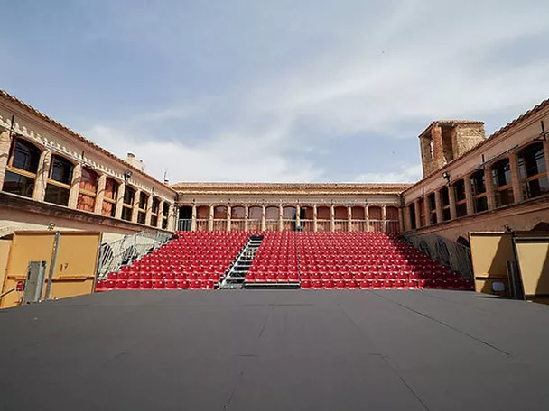 Escenario al aire libre con gradas rojas en un patio histórico vacío.