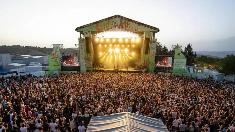 Multitud frente a un gran escenario iluminado durante un concierto al atardecer.