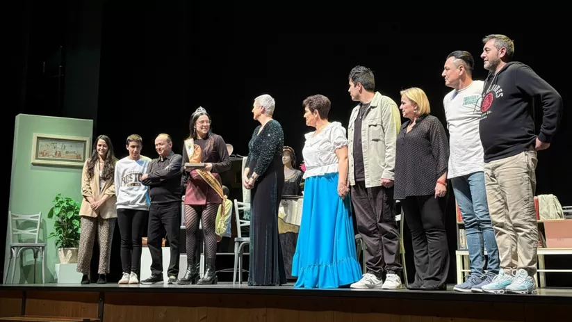 Reparto sobre el escenario saludando al público, con escenografía doméstica al fondo.