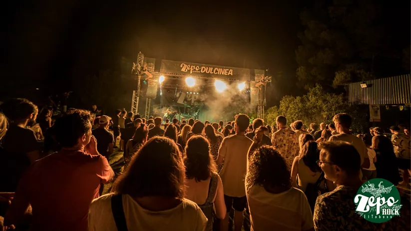 Público frente a un escenario iluminado durante un concierto nocturno al aire libre.