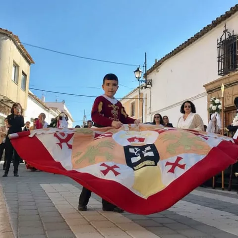 Niño portando estandarte durante procesión por calle del pueblo.