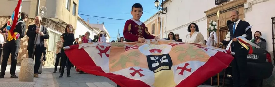 Niño portando estandarte durante procesión por calle del pueblo.
