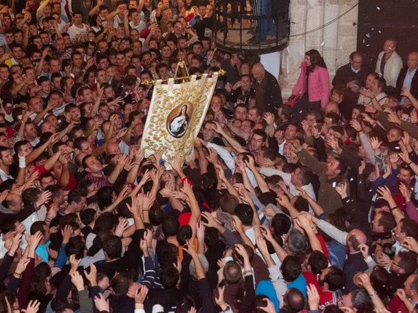 Multitud alzando un estandarte religioso en una plaza abarrotada.