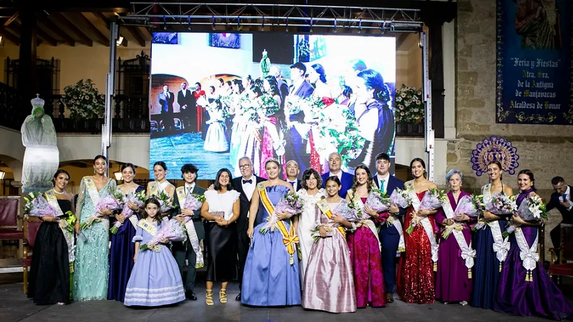 Grupo de personas vestidas de gala posando en un escenario con flores y pantalla al fondo.