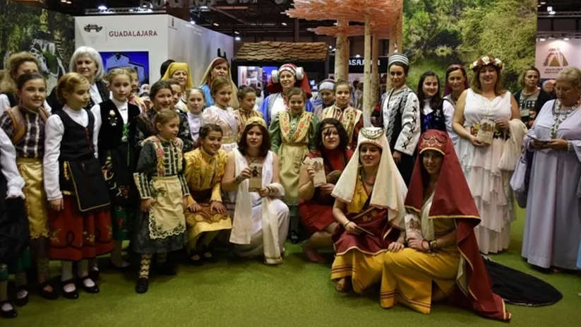 Foto de grupo en un recinto ferial, con personas vestidas con trajes tradicionales frente a un stand.