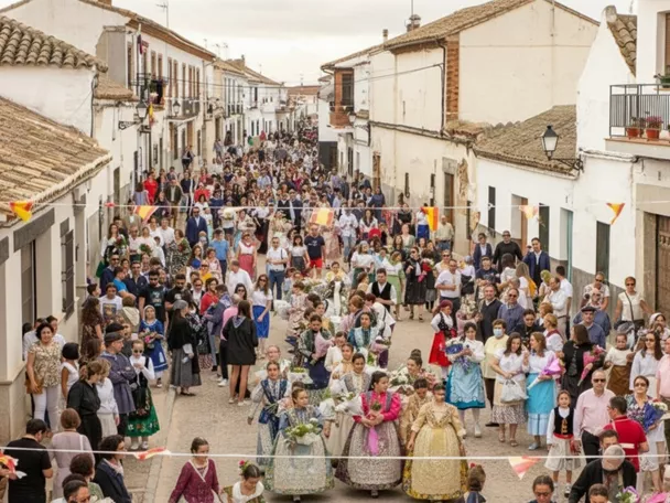 Vista elevada de una procesión multitudinaria por una calle estrecha, con participantes con flores y público a ambos lados.