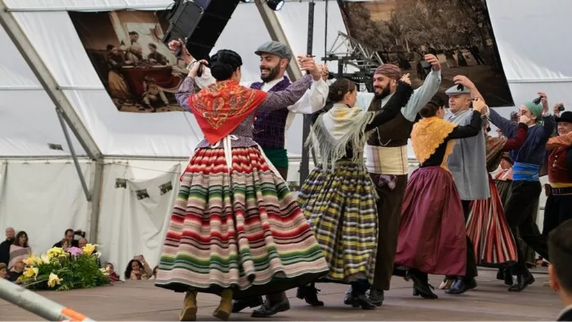 Grupo de personas con trajes tradicionales bailando en un escenario cubierto.