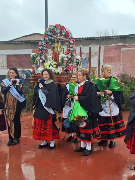 Procesión con imagen religiosa y trajes tradicionales bajo la lluvia.