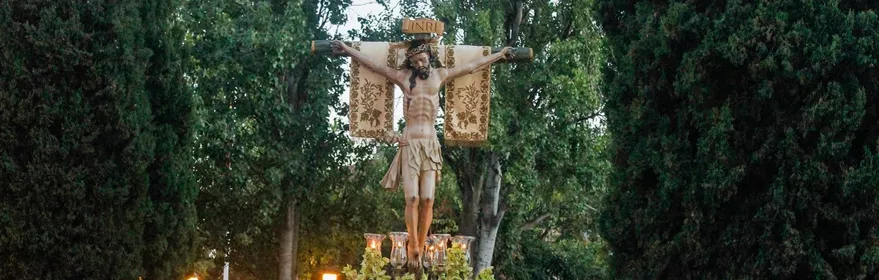 Paso procesional con imagen religiosa crucificada llevado a hombros entre una multitud.