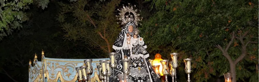Imagen religiosa iluminada con candelabros durante una procesión nocturna.