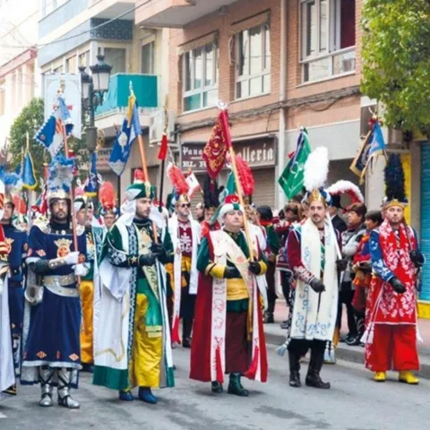 Desfile festivo con trajes históricos y estandartes en una calle urbana