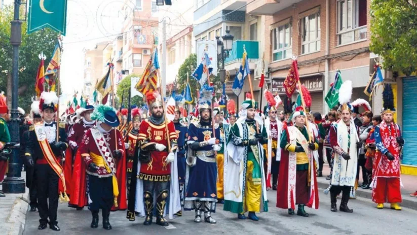 Desfile festivo con trajes históricos y estandartes en una calle urbana