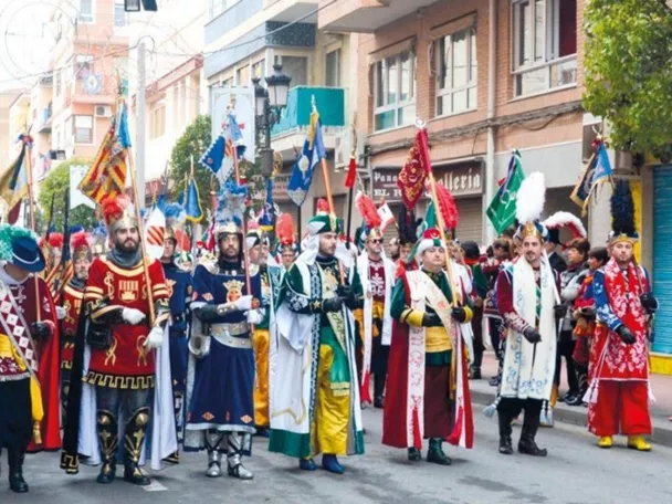 Desfile festivo con trajes históricos y estandartes en una calle urbana