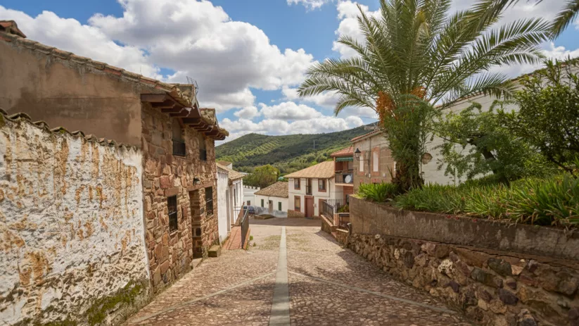 Calle empedrada de Fontanarejo (Ciudad Real) con casas de piedra y vistas a la sierra.