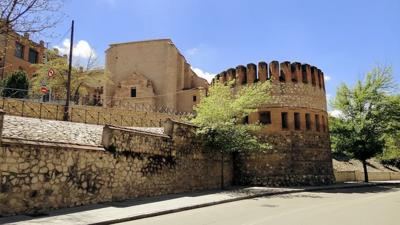 Torre defensiva circular con almenas y muro de piedra.
