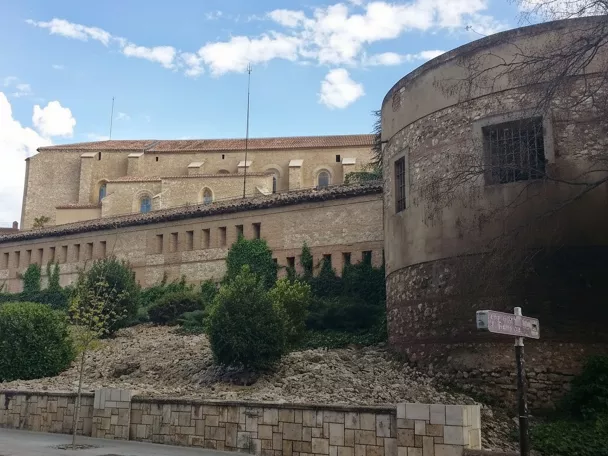 Muralla de piedra con torre circular y jardín delantero.