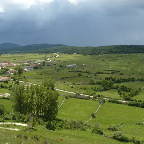 Vista panorámica de pueblo entre praderas y montañas.