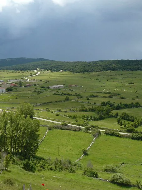 Vista panorámica de pueblo entre praderas y montañas.
