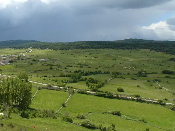 Vista panorámica de pueblo entre praderas y montañas.