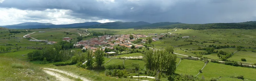 Vista panorámica de pueblo entre praderas y montañas.