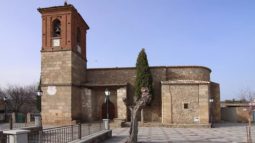 Iglesia de piedra con torre cuadrada y plaza pavimentada