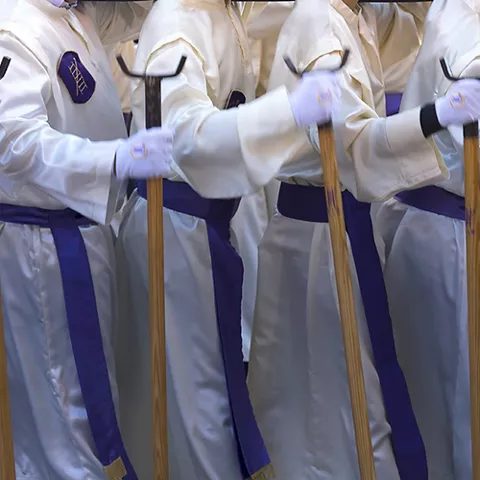 Personas con túnicas blancas y bastones en procesión nocturna