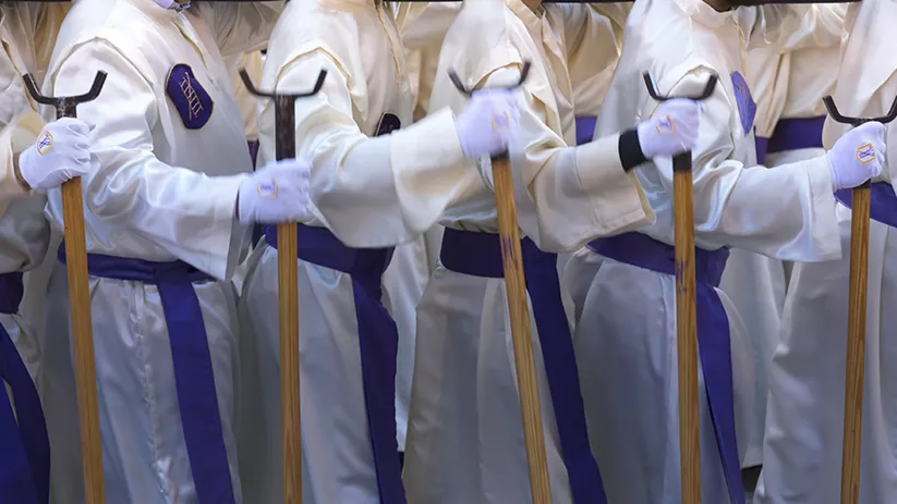 Personas con túnicas blancas y bastones en procesión nocturna