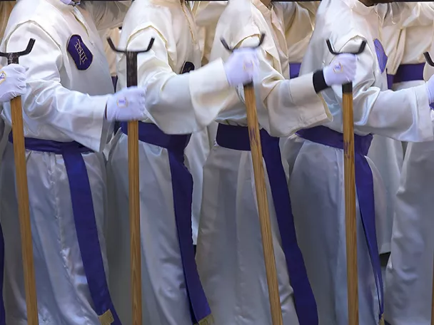 Personas con túnicas blancas y bastones en procesión nocturna