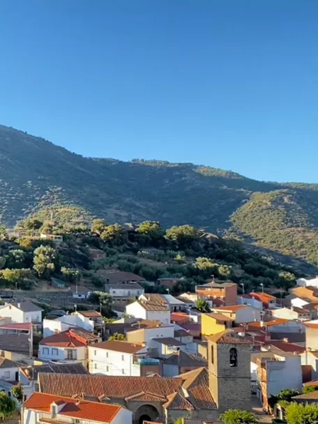 Vista del pueblo con montaña y árbol en primer plano