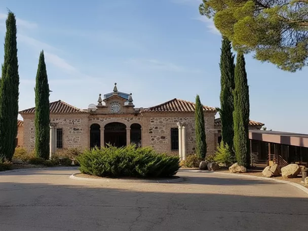 Vista frontal de edificio tradicional rodeado de árboles y jardín circular.