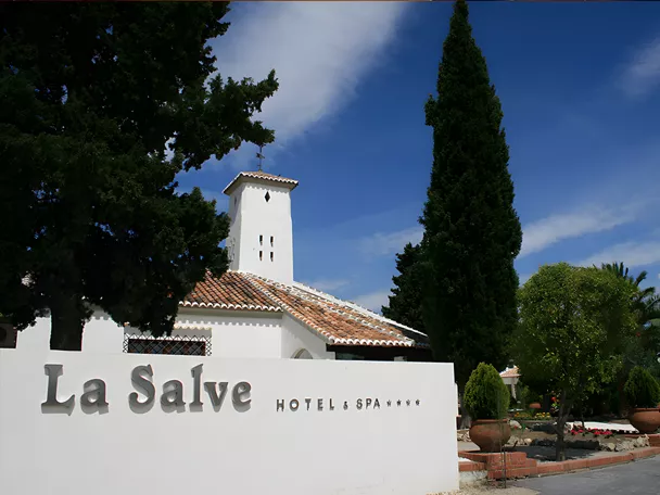 Entrada de hotel con fachada blanca, torre y jardines