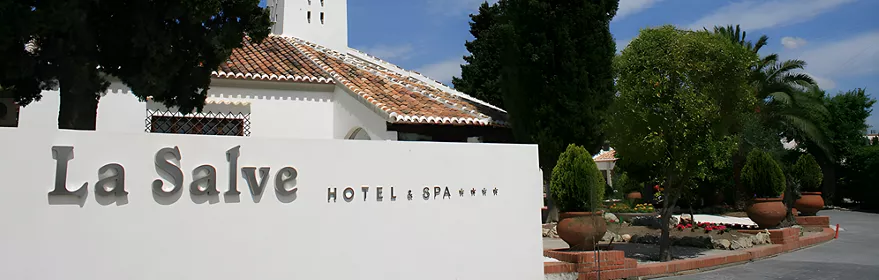 Entrada de hotel con fachada blanca, torre y jardines