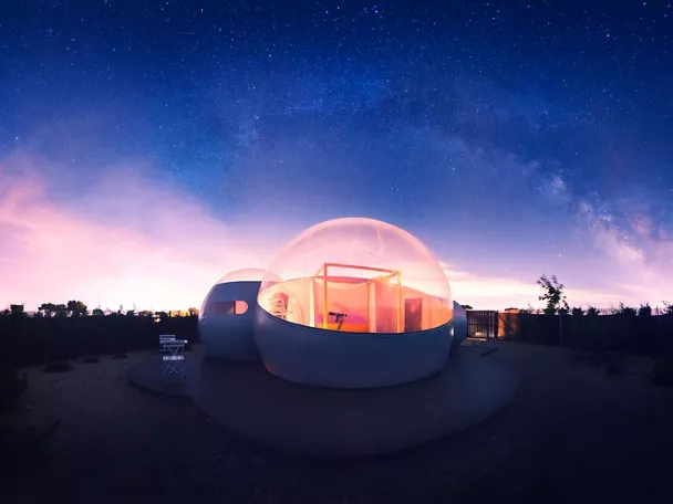 Cúpula transparente iluminada bajo un cielo nocturno lleno de estrellas.