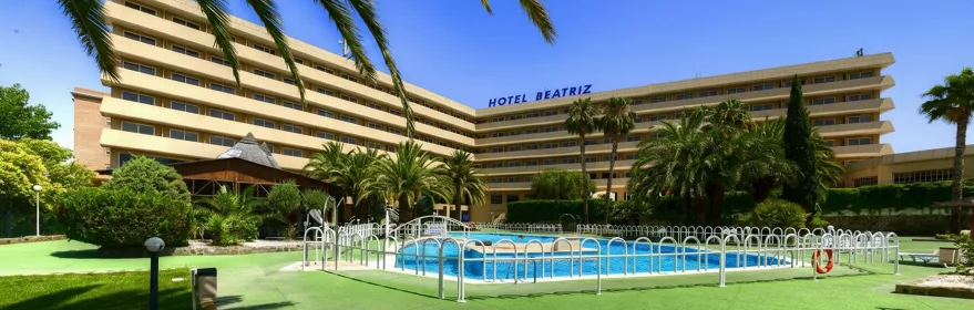 Fachada de hotel moderno con jardín de palmeras y piscina exterior.
