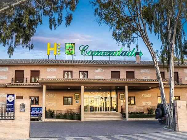 Fachada de edificio hotelero con entrada porticada y árboles en primer plano.