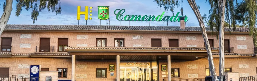 Fachada de edificio hotelero con entrada porticada y árboles en primer plano.