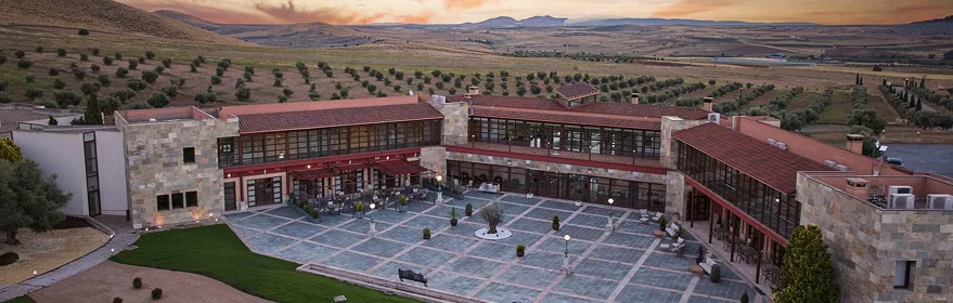 Vista aérea de un patio amplio con terrazas y edificios rodeados de campos al atardecer.