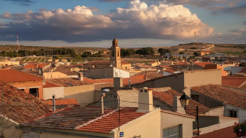 Tejados de casas tradicionales en Hoya Gonzalo con la iglesia y colinas al fondo durante el atardecer.