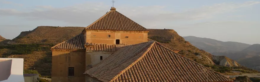 Vista de tejados de iglesia y cúpula baja, con colinas al fondo al atardecer.